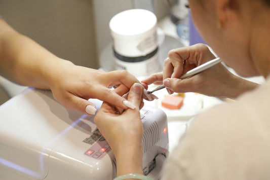 Nail technician applying acrylic nail extensions at a salon, showing the time and cost involved compared to GLITZADORA press-on nails