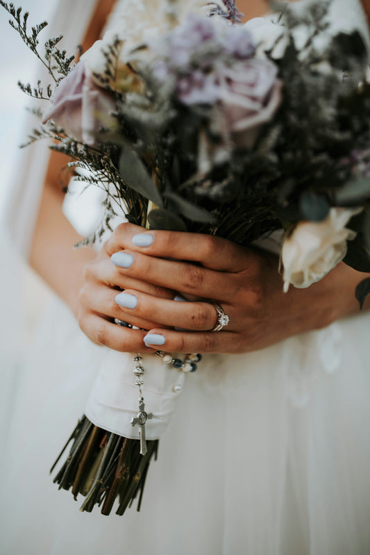 Bride holding a wedding bouquet with elegant pale green GLITZADORA press-on nails on her hands.